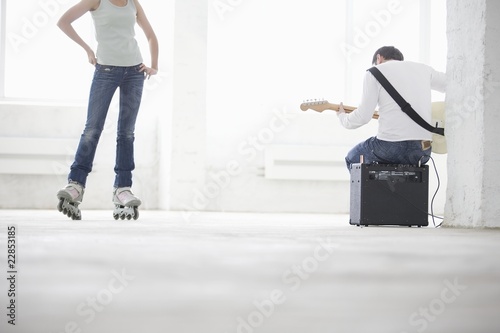 Photo: Woman on roller skates and man sitting on amp playing electric guitar Woman on roller skates and man sitting on amp playing electric guitar