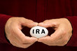 Man holds white nest egg with IRA written on it Man holds white nest egg with IRA written on it