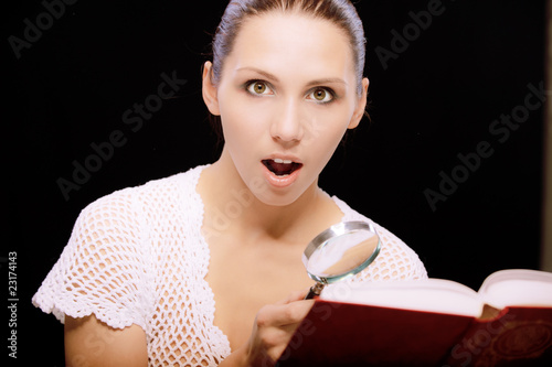Photo: Enthusiastic young woman reads book through magnifier Enthusiastic young woman reads book through magnifier