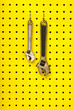 Two wrenches hang from hooks on yellow pegboard Two wrenches hang from hooks on yellow pegboard