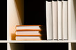 Orange and white covered books on a shelf over dark