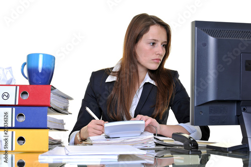 Foto: Junge Frau arbeitet im Büro zwischen Akten und PC Junge Frau arbeitet im Büro zwischen Akten und PC