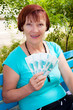 The elderly woman sits in park and holds in hands of money The elderly woman sits in park and holds in hands of money