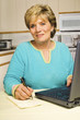 Woman writes a note while using a laptop. Woman writes a note while using a laptop.