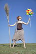 Young witch at green field with broom and wind turbine