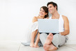 Happy young couple looking away while using laptop