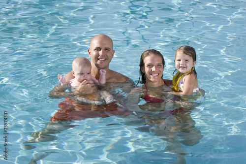 Photo: Portrait of young family smiling in swimming pool Portrait of young family smiling in swimming pool