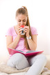 Young girl holding a cup and reading book on sofa