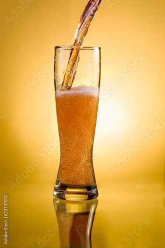Photo: Glass of beer close-up with froth over yellow background Glass of beer close-up with froth over yellow background