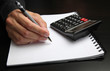 Male hand writing on a notepad with a pen, using a calculator Male hand writing on a notepad with a pen, using a calculator