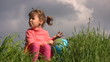 girl with terrestrial globe sits on grass against sky