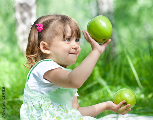 Photo: Little girl portrait with two green apples in her hands outdoor Little girl portrait with two green apples in her hands outdoor