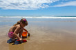 A girl playing on the wet sand with a shovel and pail