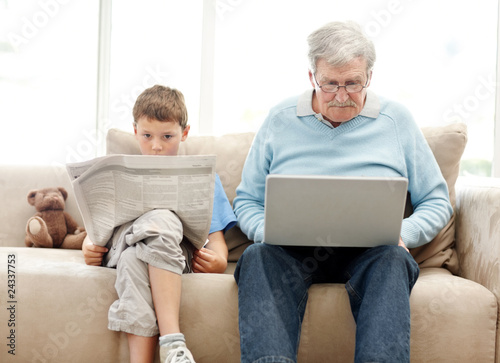 Photo: Old man using a laptop with his grand son reading a newspaper Old man using a laptop with his grand son reading a newspaper