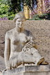 Femme de pierre assise devant un escalier monumental.