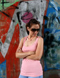 Young woman wearing sunglasses standing against graffit wall