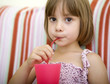 Child drinking juice sitting on her bed at home