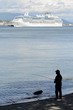 Man fishing while a ship cruises by