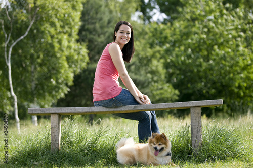 Foto: A young woman sitting on a bench, with her dog A young woman sitting on a bench, with her dog