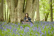 A young woman sitting under a tree, holding a picnic basket