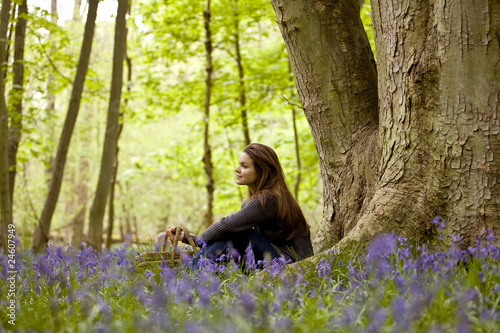Foto: A young woman sitting under a tree, holding a picnic basket A young woman sitting under a tree, holding a picnic basket