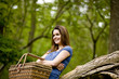 A young woman leaning against a tree, holding a picnic basket