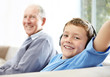 Small boy enjoying music on headphones with grandfather in backg
