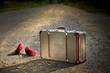 Old suitcase with red shoes left on road