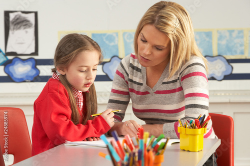 Photo: Female Primary School Pupil And Teacher Working At Desk In Class Female Primary School Pupil And Teacher Working At Desk In Class