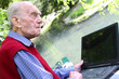 Alter Mann arbeitet mit dem Laptop im Grünen am Wasser Alter Mann arbeitet mit dem Laptop im Grünen am Wasser