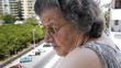 Old retired woman watching traffic from balcony