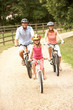 Family Cycling In Countryside Wearing Safety Helmets