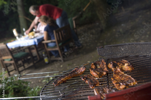 Photo: BBq with meat in foreground people in background BBq with meat in foreground people in background