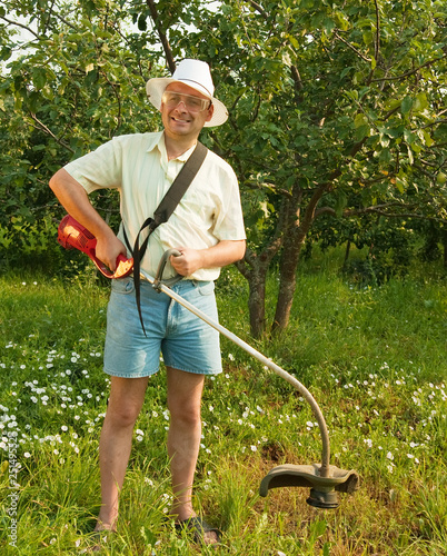 Photo: man works with cordless grass trimmer man works with cordless grass trimmer