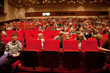 Adults and children sit on red chairs in auditorium
