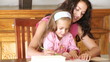 mother writing with her daughter on her knees