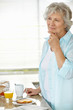 Thoughtful senior woman at kitchen while having her breakfast
