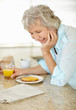 Happy mature woman having her breakfast while reading newspaper
