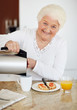 Woman pouring coffee in cup while having breakfast