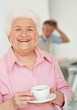 Elderly female holding a cup of tea with blur man in background