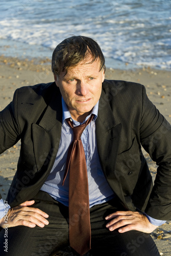 Wet and depressed businessman sitting on the beach. Wet and depressed businessman sitting on the beach.