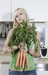 germany, berlin, young woman in kitchen holding bunch of carrots, portrait