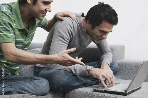 Photo: men sitting on couch using laptop, smiling. men sitting on couch using laptop, smiling.
