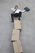 Photo: businessman balancing on stack of cardboard boxes, using mobile phone, elevated view businessman balancing on stack of cardboard boxes, using mobile phone, elevated view