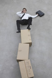 Photo: businessman balancing on stack of cardboard boxes, using mobile phone, elevated view businessman balancing on stack of cardboard boxes, using mobile phone, elevated view