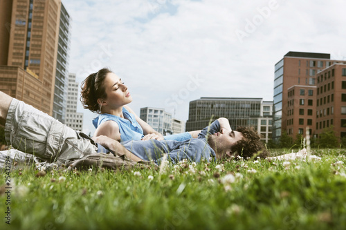 Foto: germany, berlin, young couple lying in meadow, high rise buildings in background germany, berlin, young couple lying in meadow, high rise buildings in background