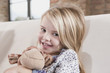 germany, cologne, girl (4-5) with a stuffed toy, sitting on sofa