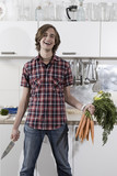 Photo: germany, berlin, young man in kitchen holding bunch of carrots and knife, laughing, portrait germany, berlin, young man in kitchen holding bunch of carrots and knife, laughing, portrait