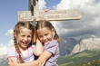 Photo: italy, seiseralm, girls (6-7), (8-9) standing by sign post, smiling, portrait, close-up italy, seiseralm, girls (6-7), (8-9) standing by sign post, smiling, portrait, close-up