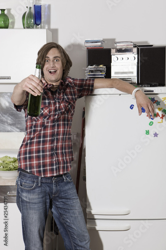 Photo: germany, berlin, young man in kitchen holding beer bottle, portrait germany, berlin, young man in kitchen holding beer bottle, portrait